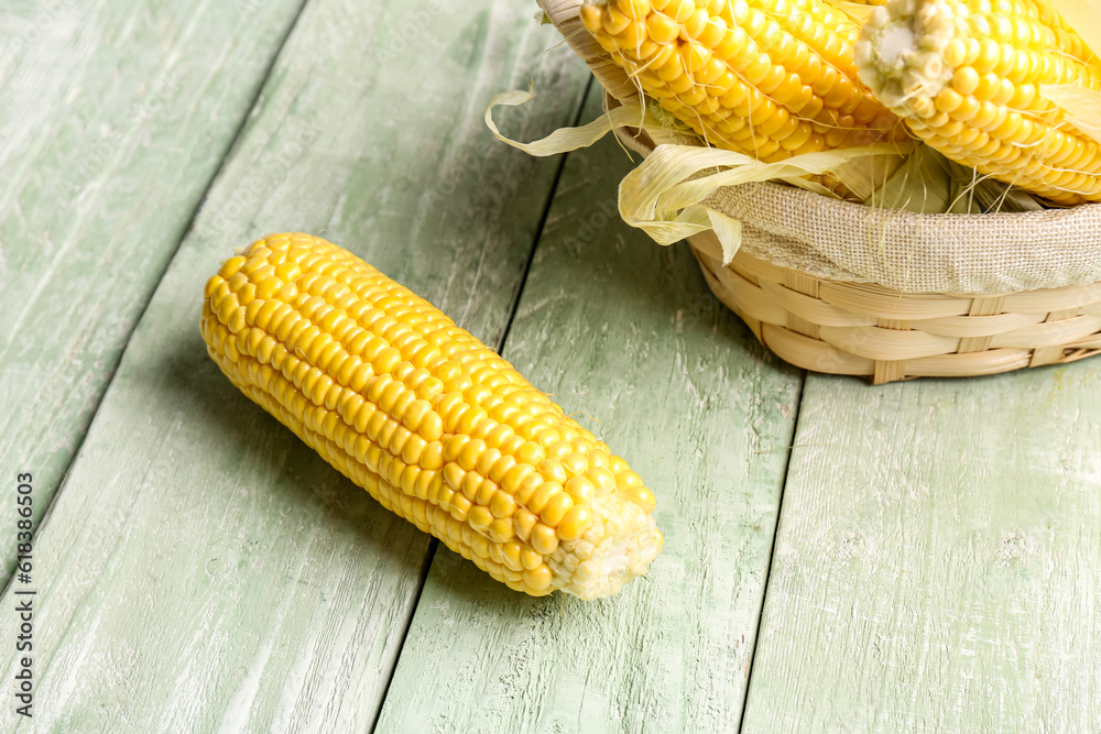 Wicker bowl with fresh corn cobs on green wooden background