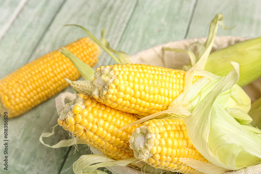 Wicker bowl with fresh corn cobs on green wooden background