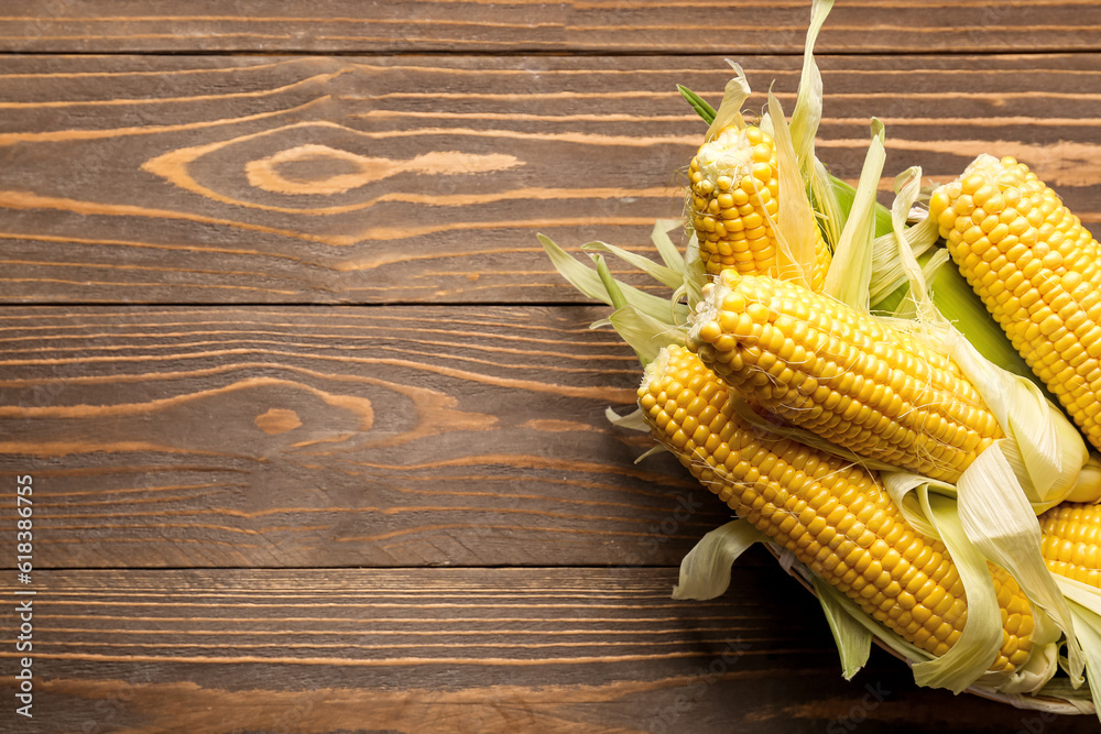 Wicker bowl with fresh corn cobs on wooden background