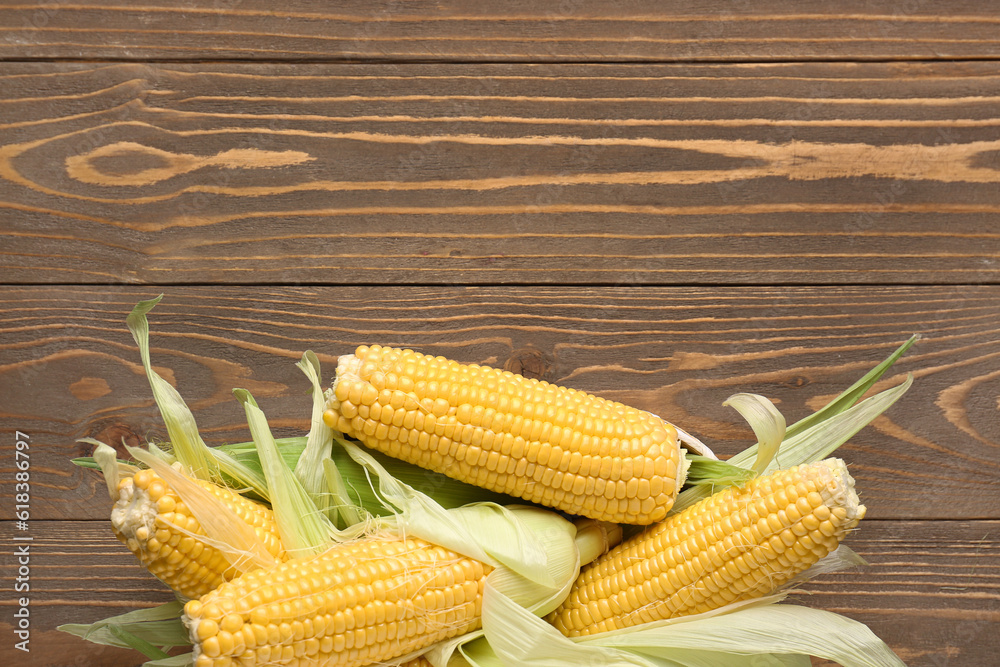 Wicker bowl with fresh corn cobs on wooden background