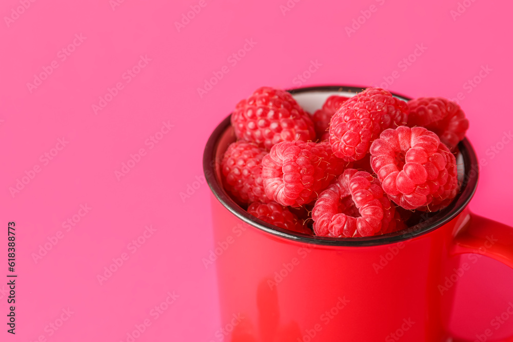 Cup with fresh raspberries on pink background