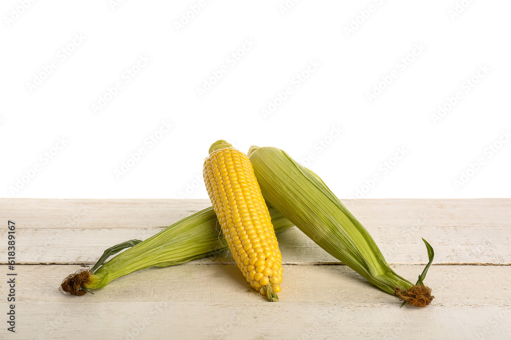 Fresh corn cobs on light wooden table against white background