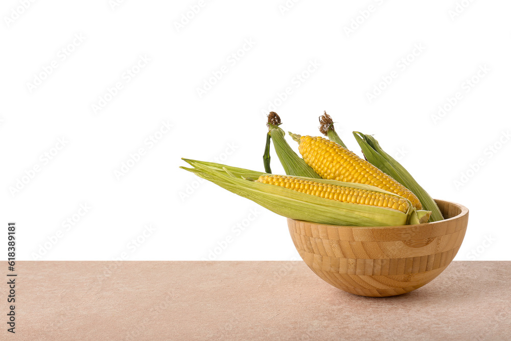 Bowl with fresh corn cobs on pink table against white background