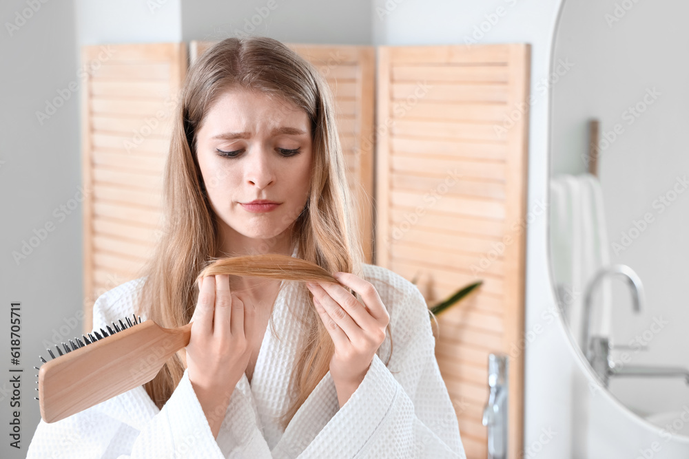 Upset young woman with hair loss problem and brush in bathroom