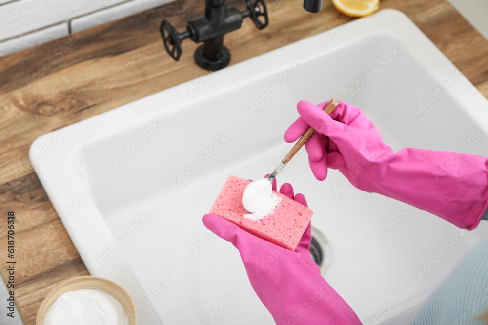 Woman in rubber gloves cleaning white sink with sponge and baking soda, closeup