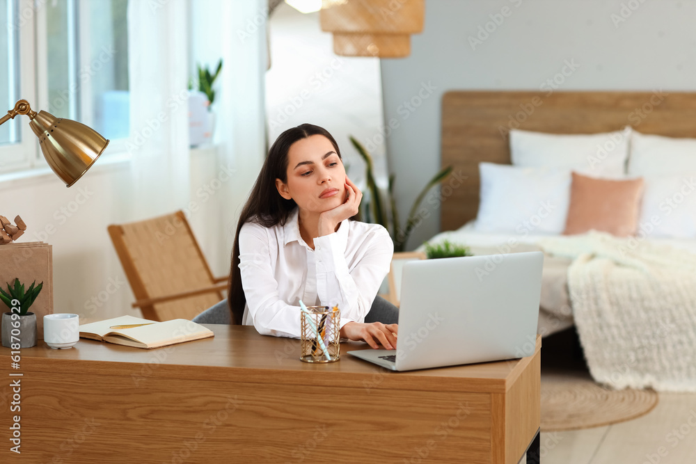 Thoughtful young woman sitting at table in bedroom