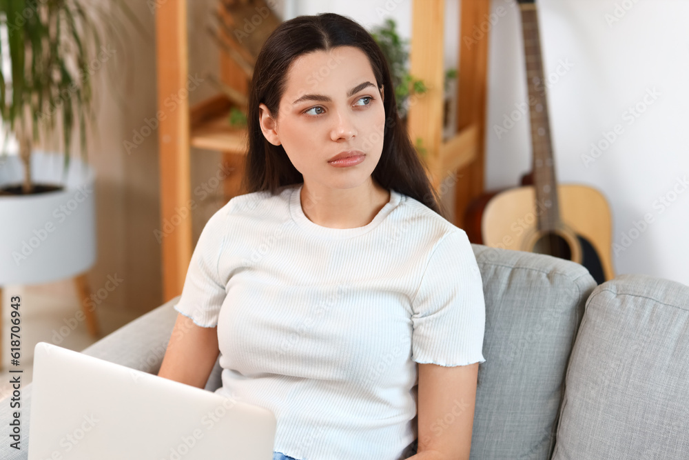 Thoughtful young woman with laptop on sofa at home