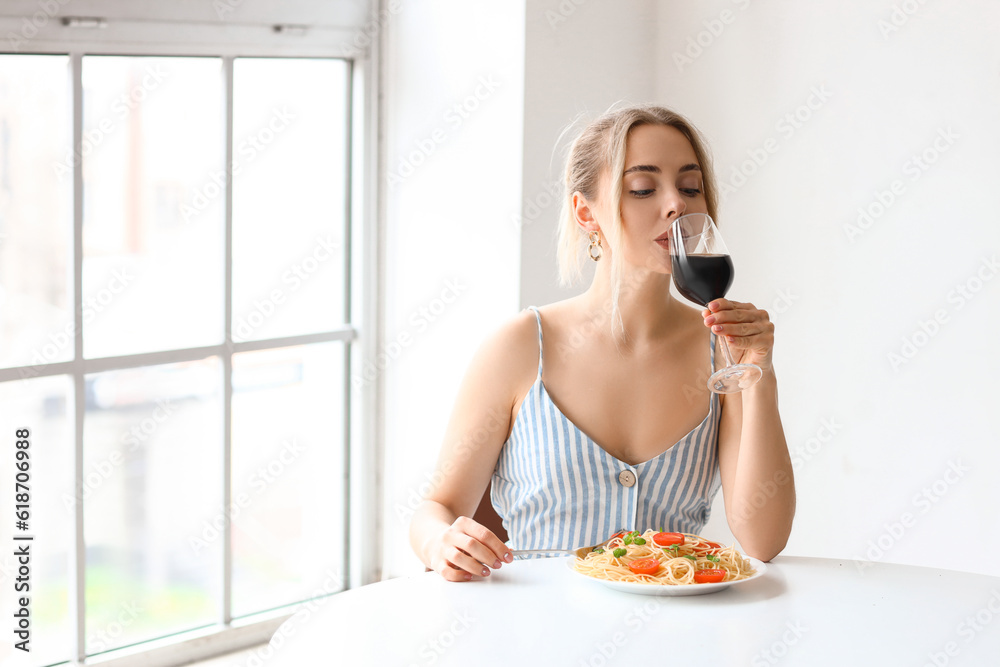 Young woman with tasty pasta drinking wine at table in restaurant