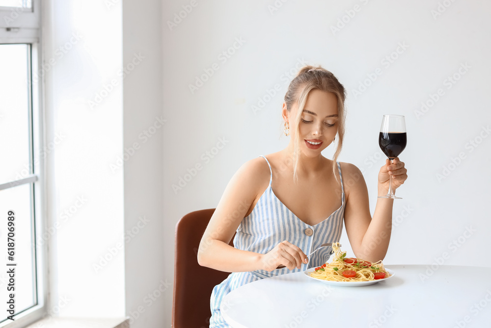 Young woman with tasty pasta and glass of wine sitting at table in restaurant