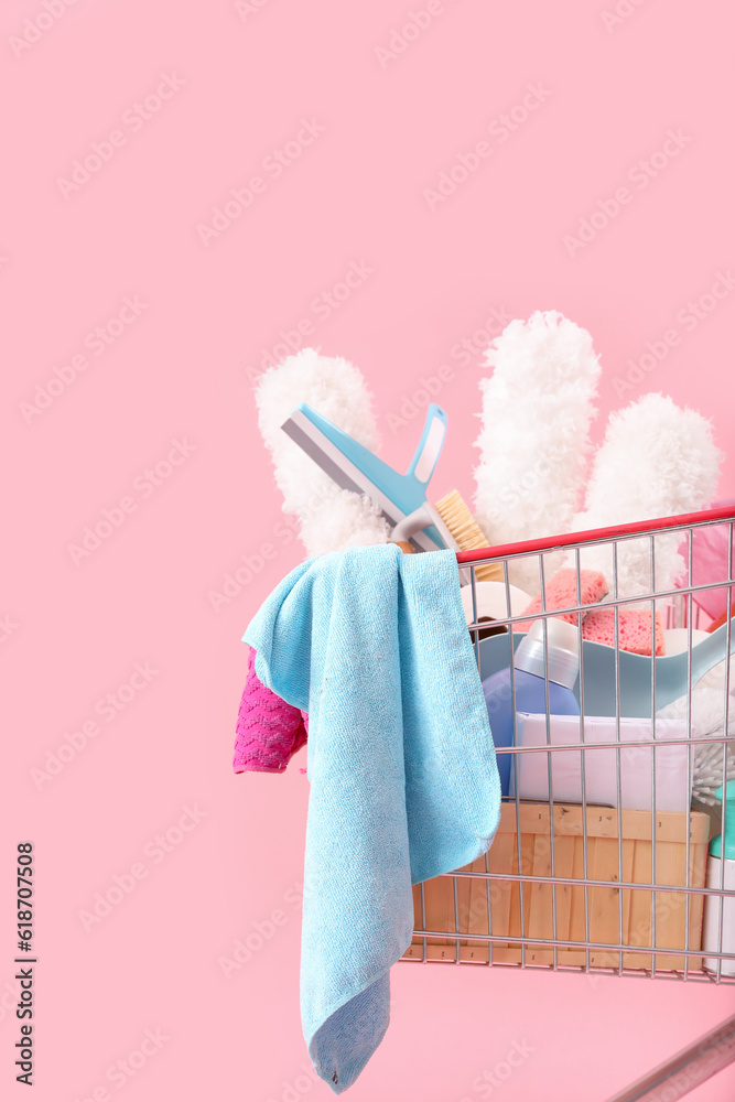 Shopping cart full of cleaning supplies on pink background