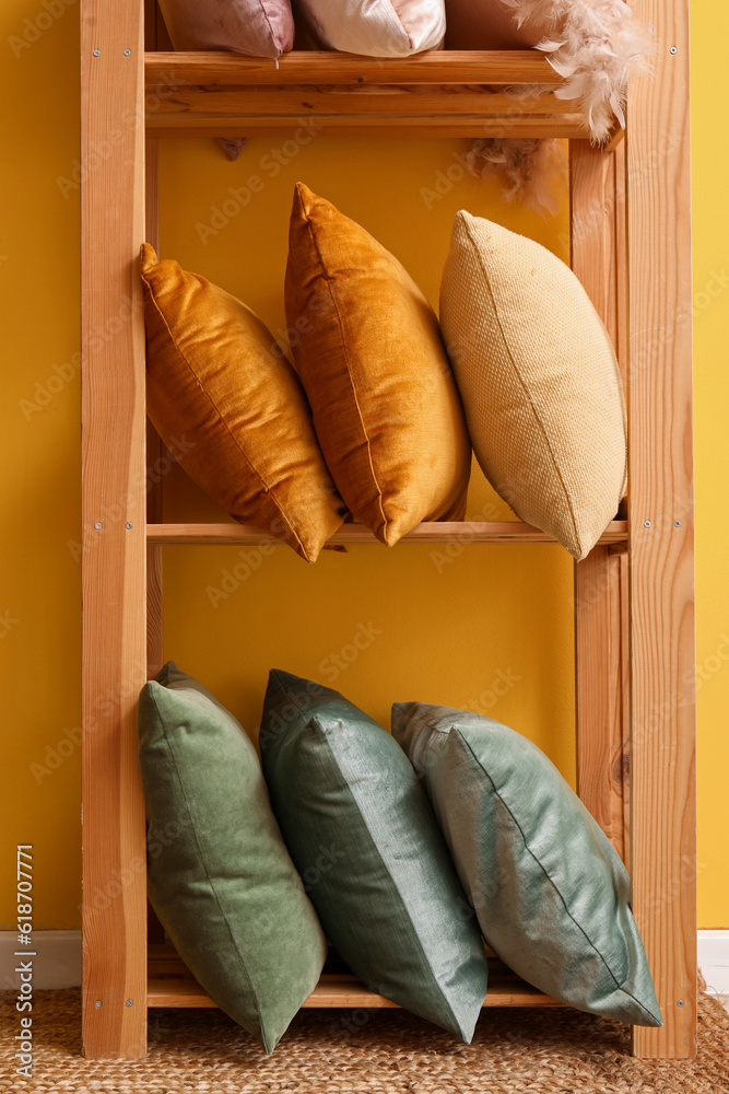 Shelving unit with stylish pillows near yellow wall in room