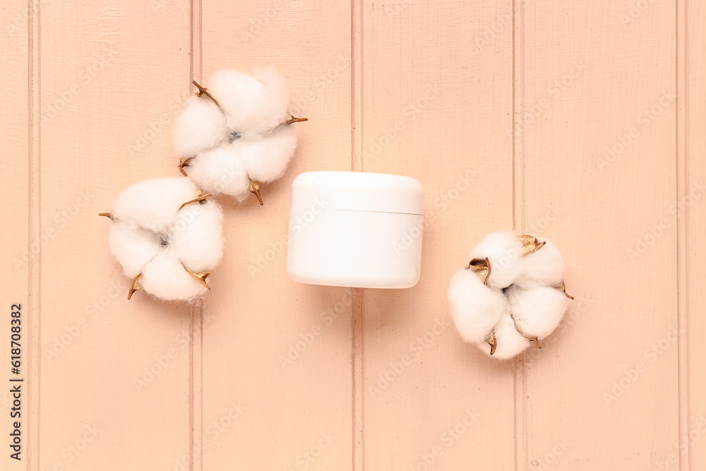 Jar of cosmetic product and cotton flowers on color wooden background