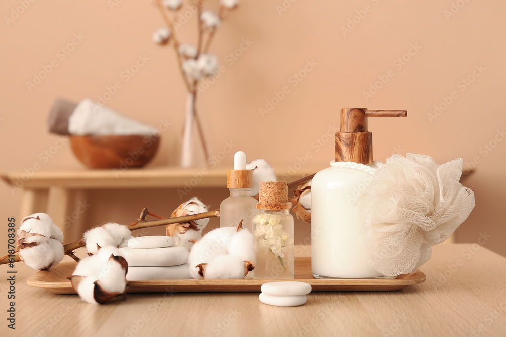 Cosmetic products, bath sponge, spa stones and cotton branch on wooden table near color wall