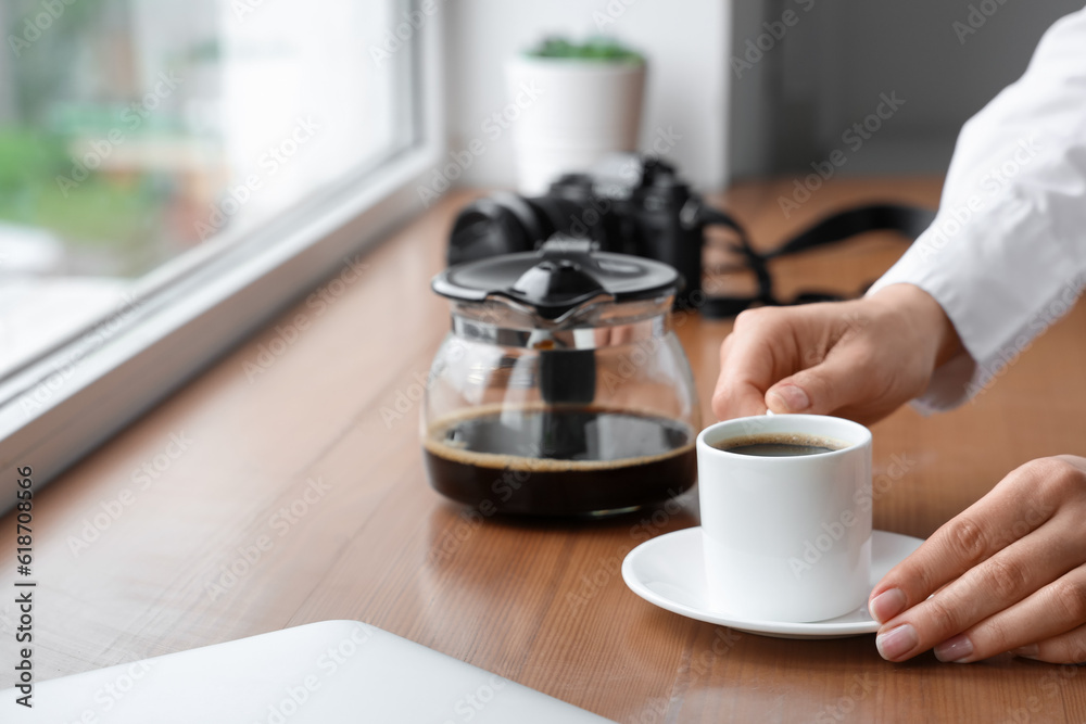 Woman holding cup of delicious coffee on windowsill