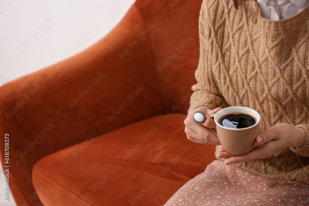 Woman sitting on cozy sofa and holding cup of delicious coffee