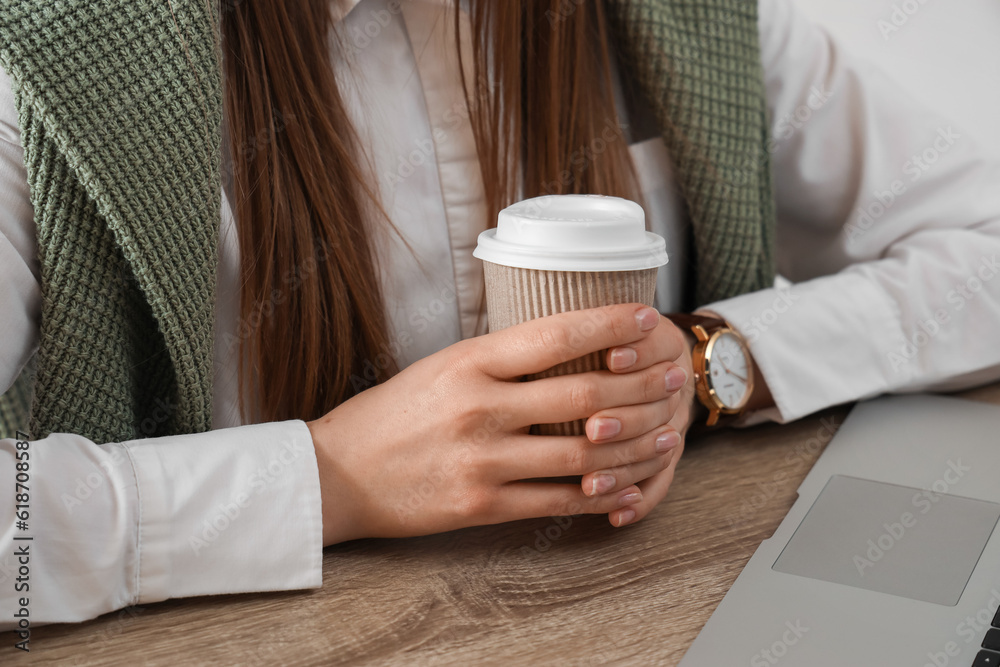 Woman holding takeaway cup of coffee at table with modern laptop