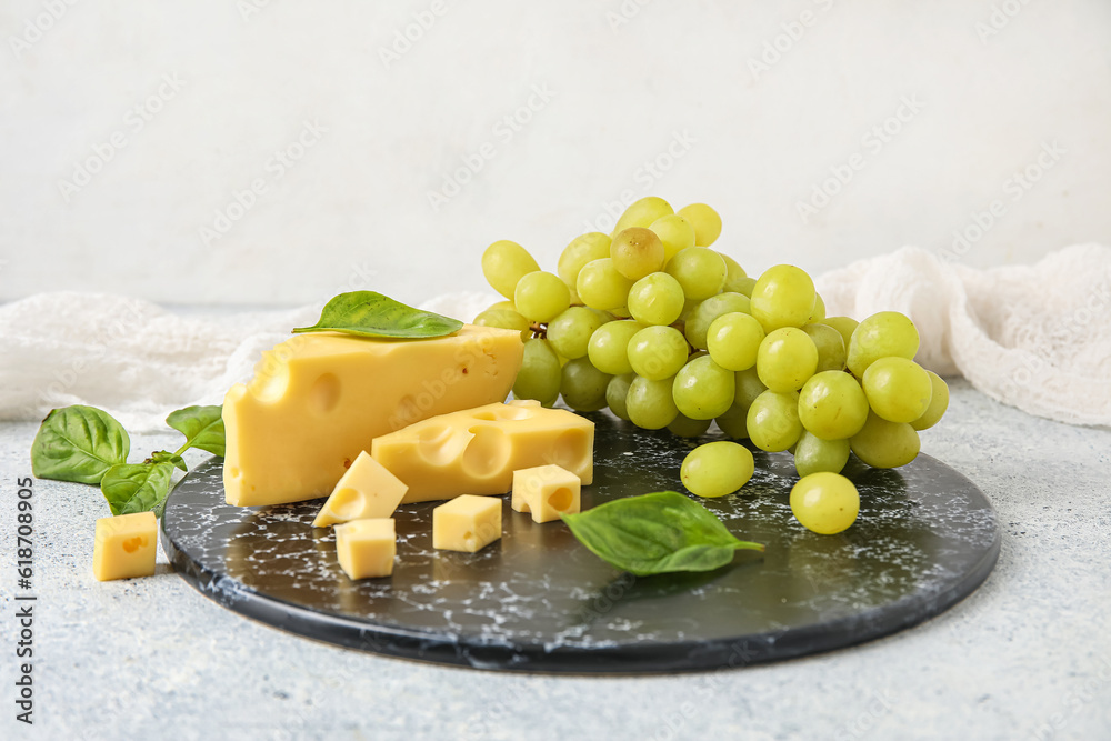 Board with tasty Swiss cheese and grapes on light background