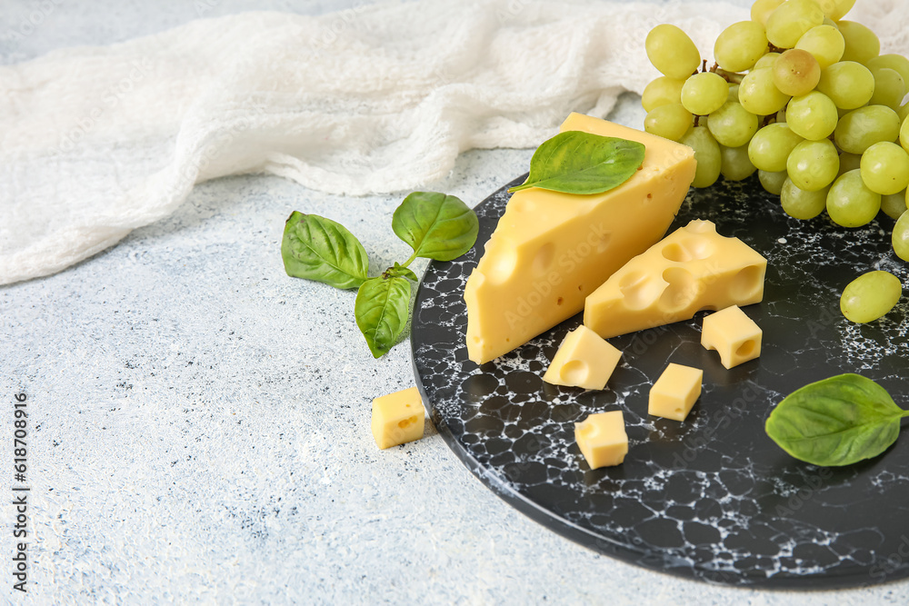 Board with tasty Swiss cheese and grapes on light background