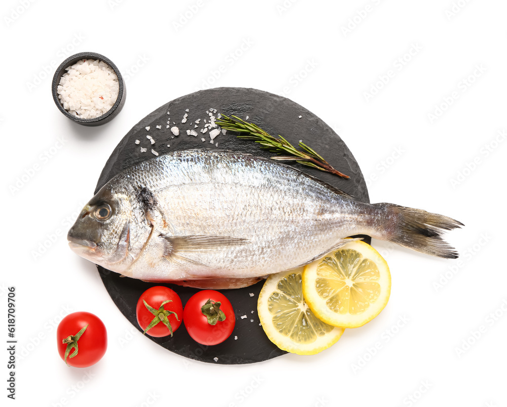 Slate board of raw dorado fish with lemon and tomatoes on white background