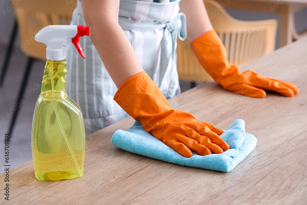 Woman in orange rubber gloves cleaning wooden countertop with rag and detergent