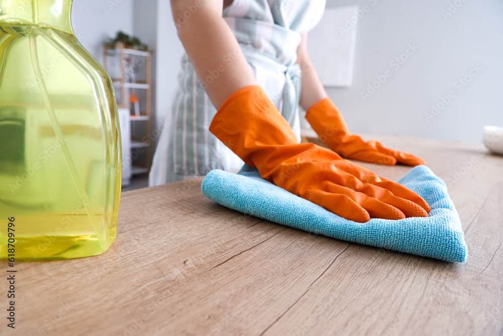 Woman in orange rubber gloves cleaning wooden countertop with rag