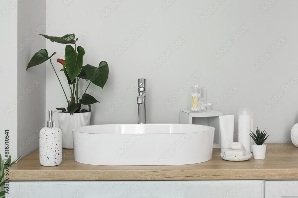 Sink bowl and bath accessories on wooden counter in bathroom