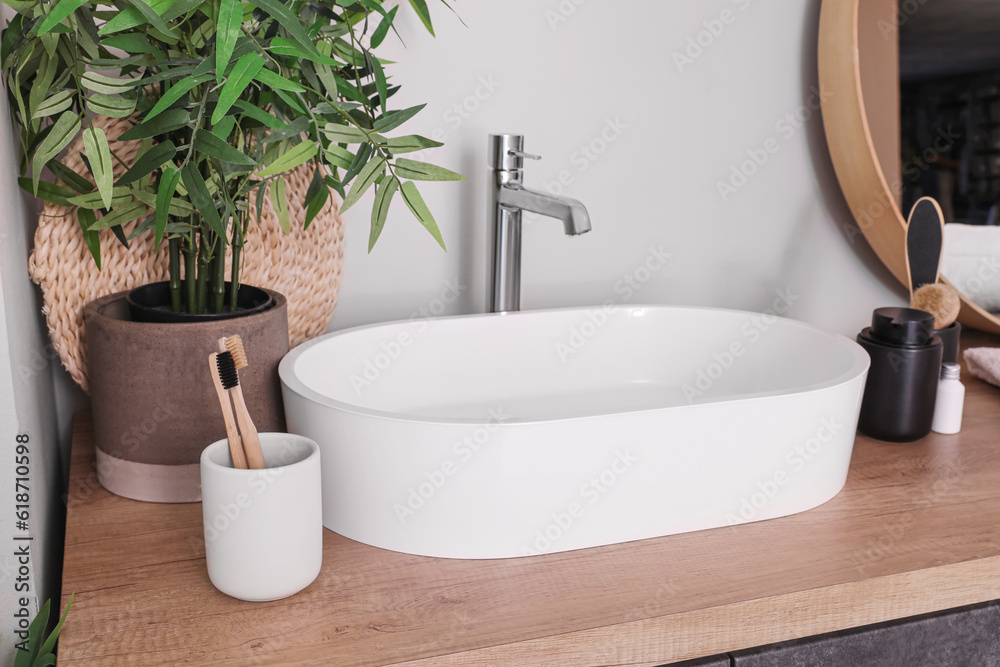 Sink bowl and bath accessories on wooden counter in bathroom