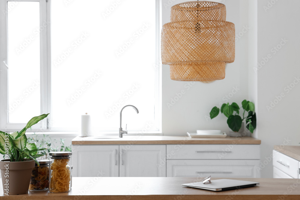 Modern laptop and eyeglasses on wooden kitchen counter in light kitchen