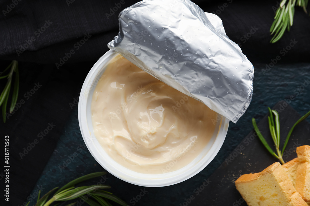 Plastic container with tasty cream cheese on black background