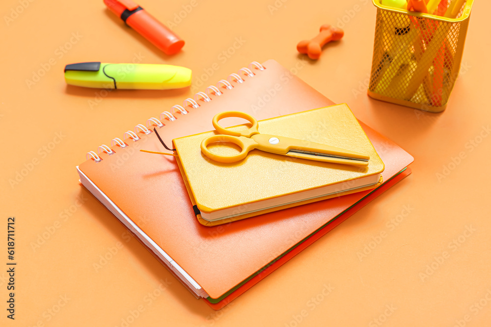 Notebooks with different stationery on orange background, closeup