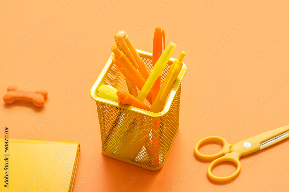 Cup with school stationery on orange background, closeup