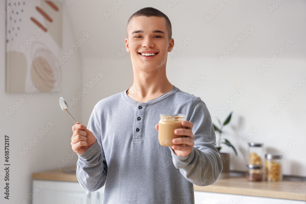 Happy young man with tasty nut butter in kitchen