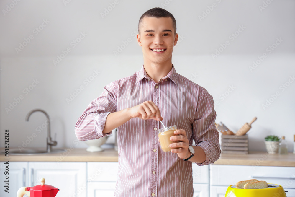 Happy young man with tasty nut butter in kitchen