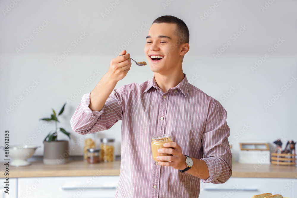 Young man eating tasty nut butter in kitchen