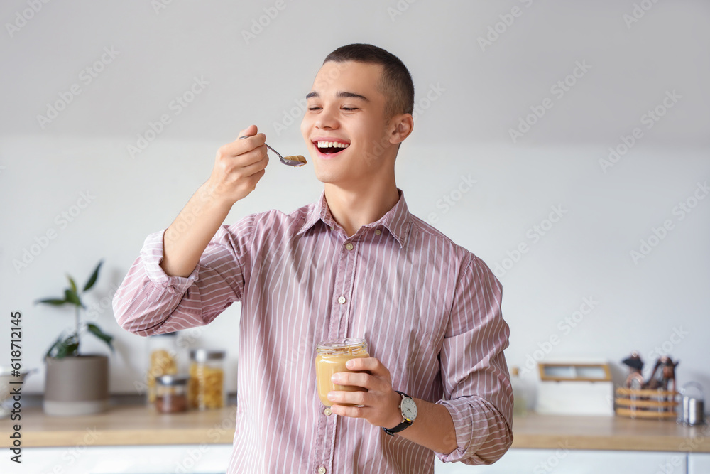 Young man eating tasty nut butter in kitchen