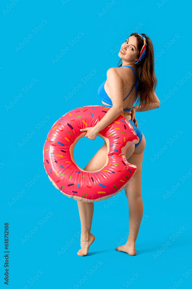 Young woman with swim ring in shape of doughnut on blue background