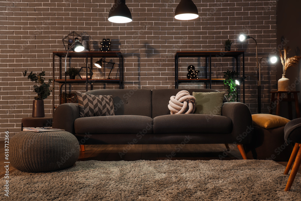 Interior of dark living room with cozy grey sofa and glowing lamps