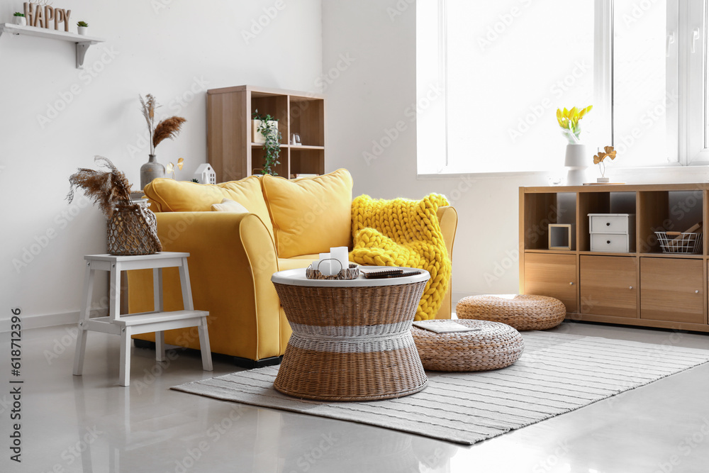 Interior of light living room with stylish yellow sofa, coffee table and wicker poufs