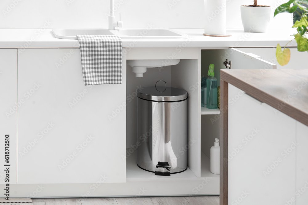 Metallic trash bin inside white counter in modern kitchen