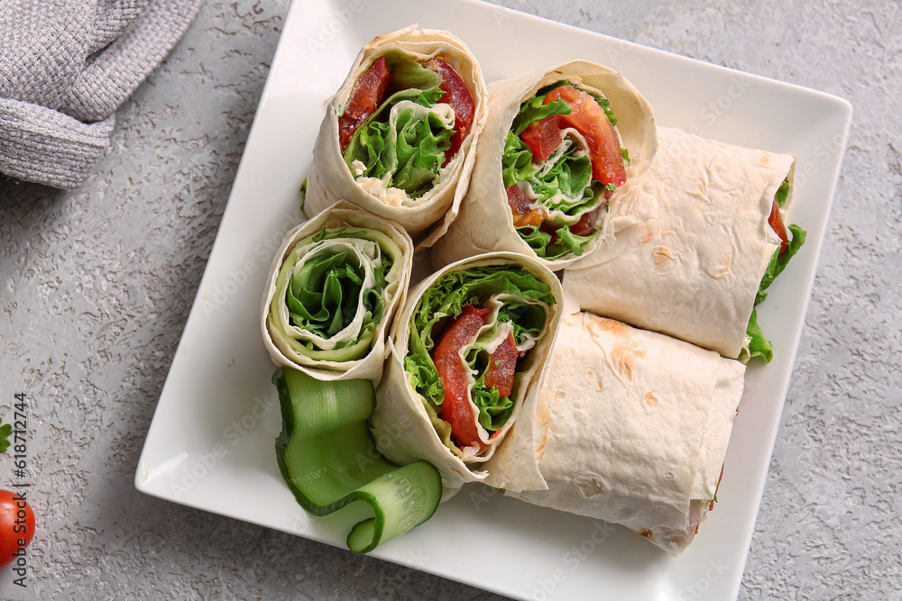 Plate of tasty lavash rolls with vegetables on grey background