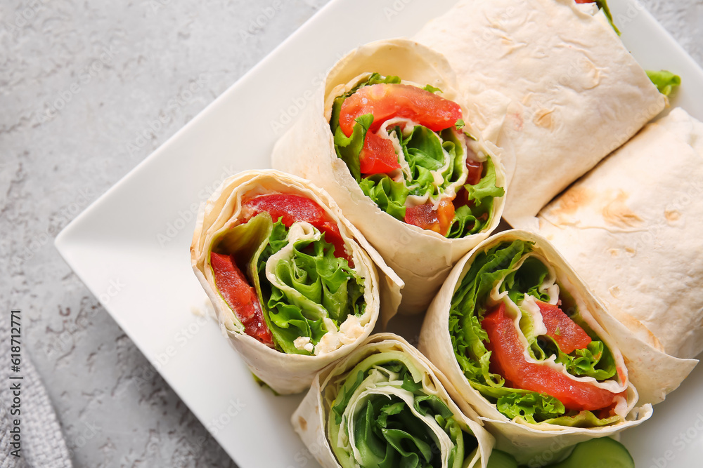 Plate of tasty lavash rolls with vegetables on grey background