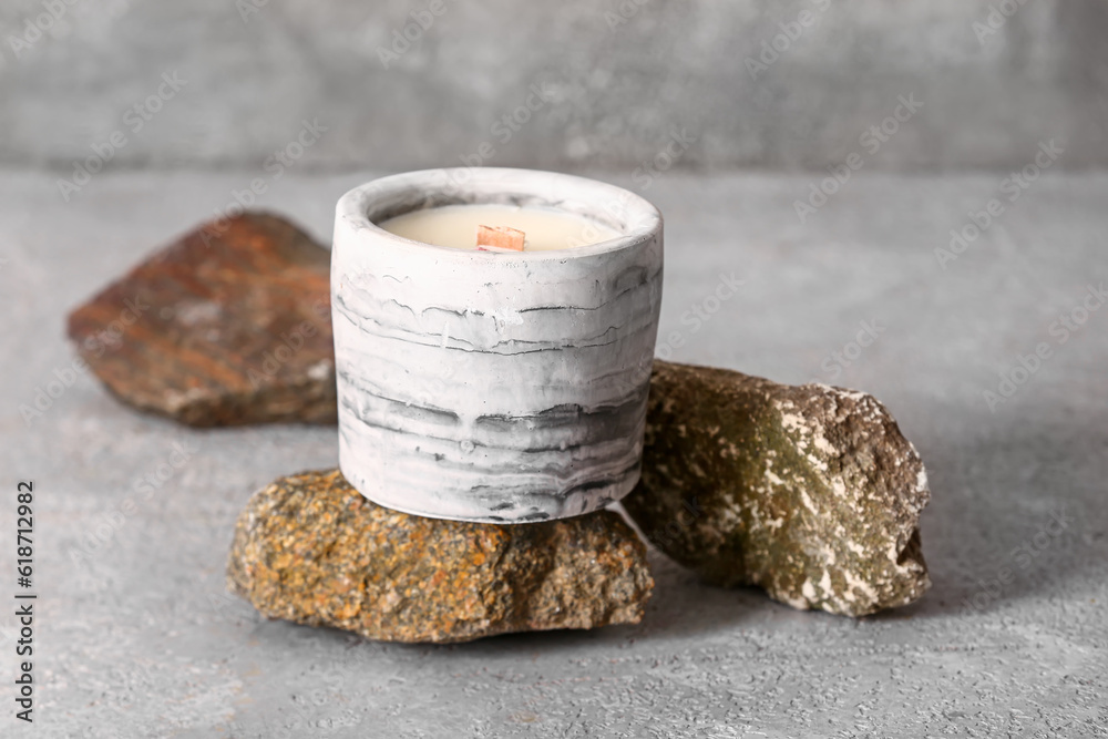 Holder with candle and stones on grey background