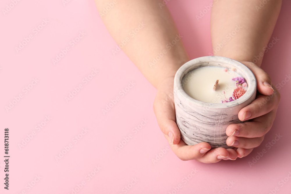 Female hands holding candle with flowers on pink background