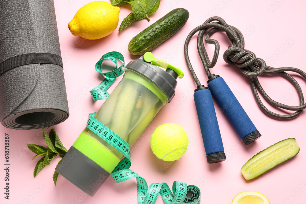 Bottle of lemonade with cucumber and sport equipment on pink background