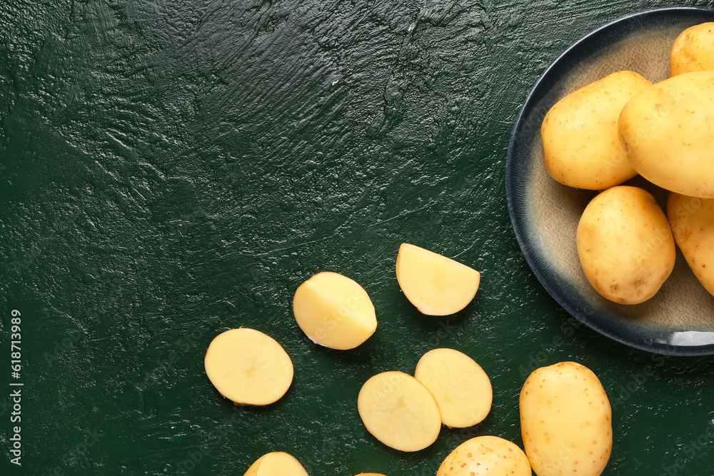 Plate with raw baby potatoes on green background