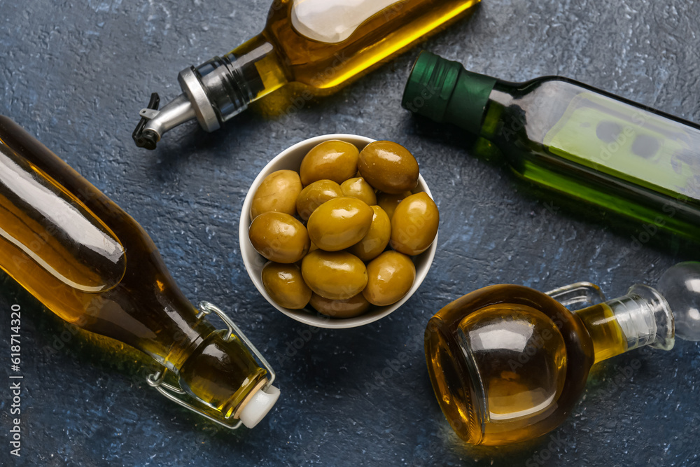 Bowl with ripe olives and bottles of oil on blue background