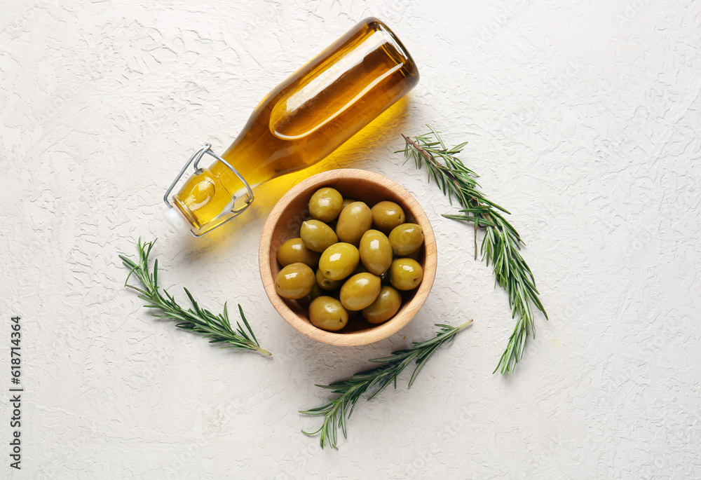 Bowl with ripe olives and bottle of oil on light background