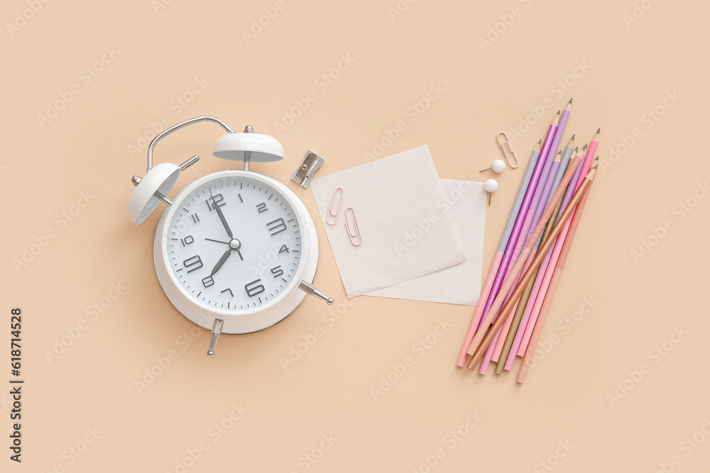 Alarm clock with different stationery on pale orange background