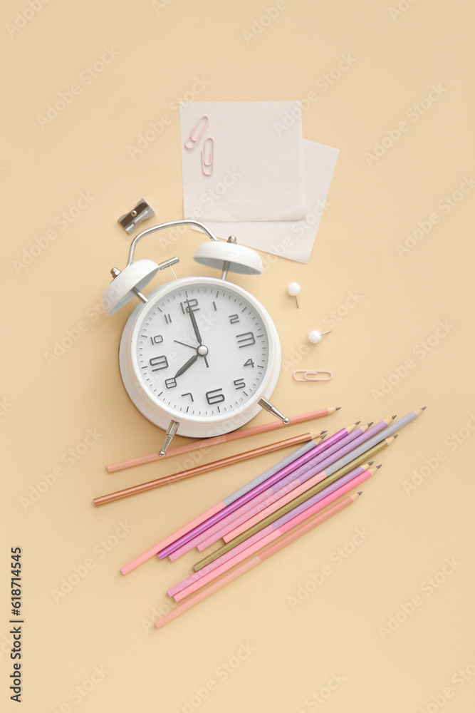 Alarm clock with different stationery on pale orange background