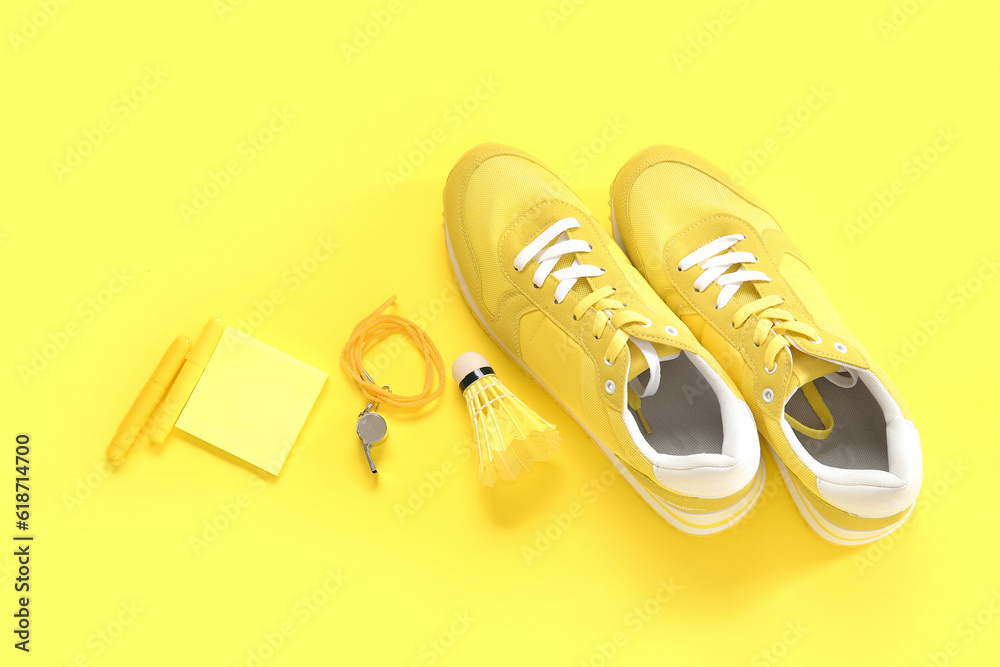 Sneakers with whistle, shuttlecock and stationery on yellow background